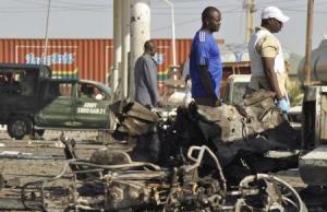 A military vehicle and people pass site of an explosion at a police station in Kano