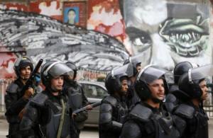 Riot police walk in front of graffiti depicting Bassem Mohsen along Mohamed Mahmoud street  during the third anniversary of violent and deadly clashes near Tahrir Square in Cairo