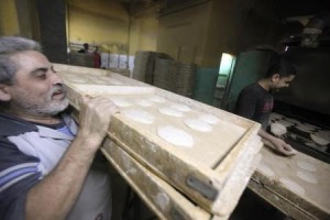 A worker carries trays of bread to be baked in an oven at a bakery in Cairo