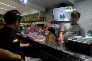 Men stand in a store as  Thailand Prime Minister Prayuth Chan-ocha is seen on a TV during his weekly broadcast in Bangkok 