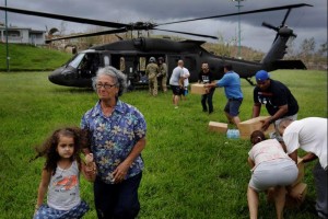 A woman and child walk away as soldiers in a UH-60 Blackhawk helicopter from the First Armored Division's Combat Aviation Brigade deliver food and water during recovery efforts following Hurricane Maria in Verde de Comerio, Puerto Rico, 